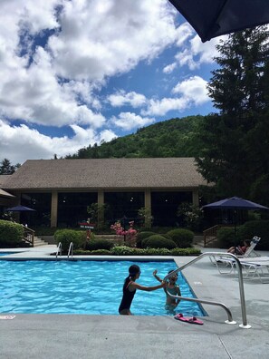A swimming pool with two people in the water, surrounded by lounge chairs and umbrellas. - Cozy Cabin with fireplace and screened in porch in Sapphire Valley. (Sapphire)