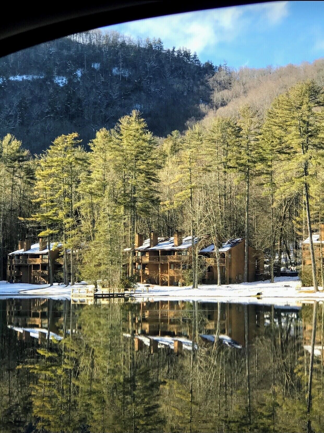 A lodge with multiple buildings surrounded by dense forest and a lake.