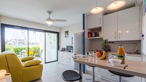 Una cocina moderna con armarios blancos, un comedor con mobiliario amarillo y vistas al exterior a través de grandes puertas de vidrio.