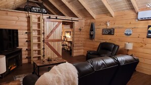 A cozy log cabin interior with a fireplace, a leather sofa, a ladder, and a mounted television. - Secluded East TN Log Cabin (Ten Mile)