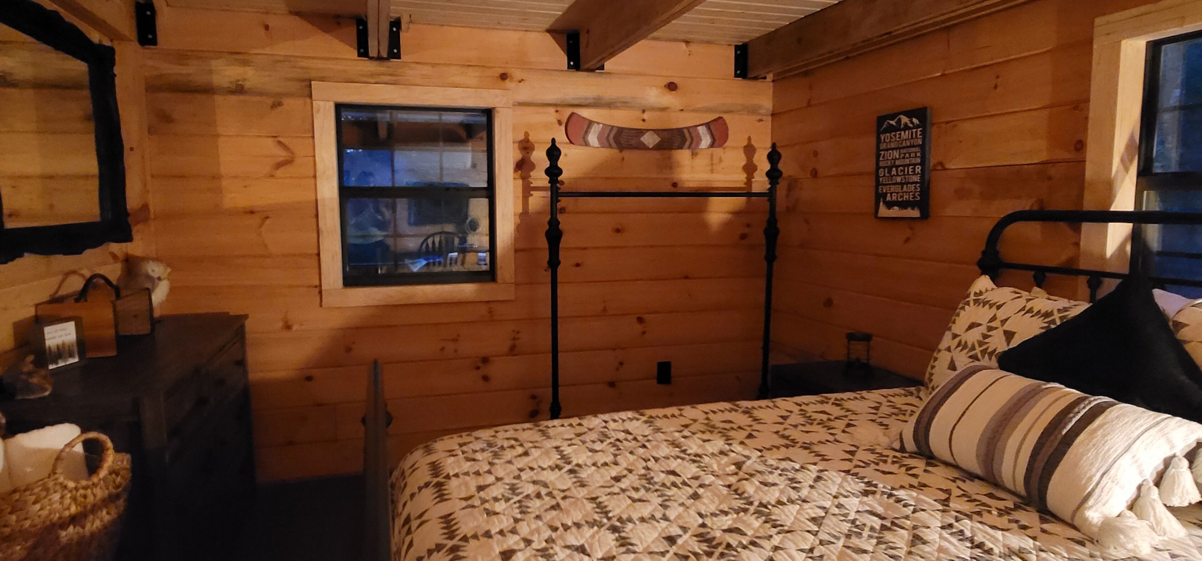 A wooden cabin room with a bed, a window, a wall-mounted sign, and a small table.