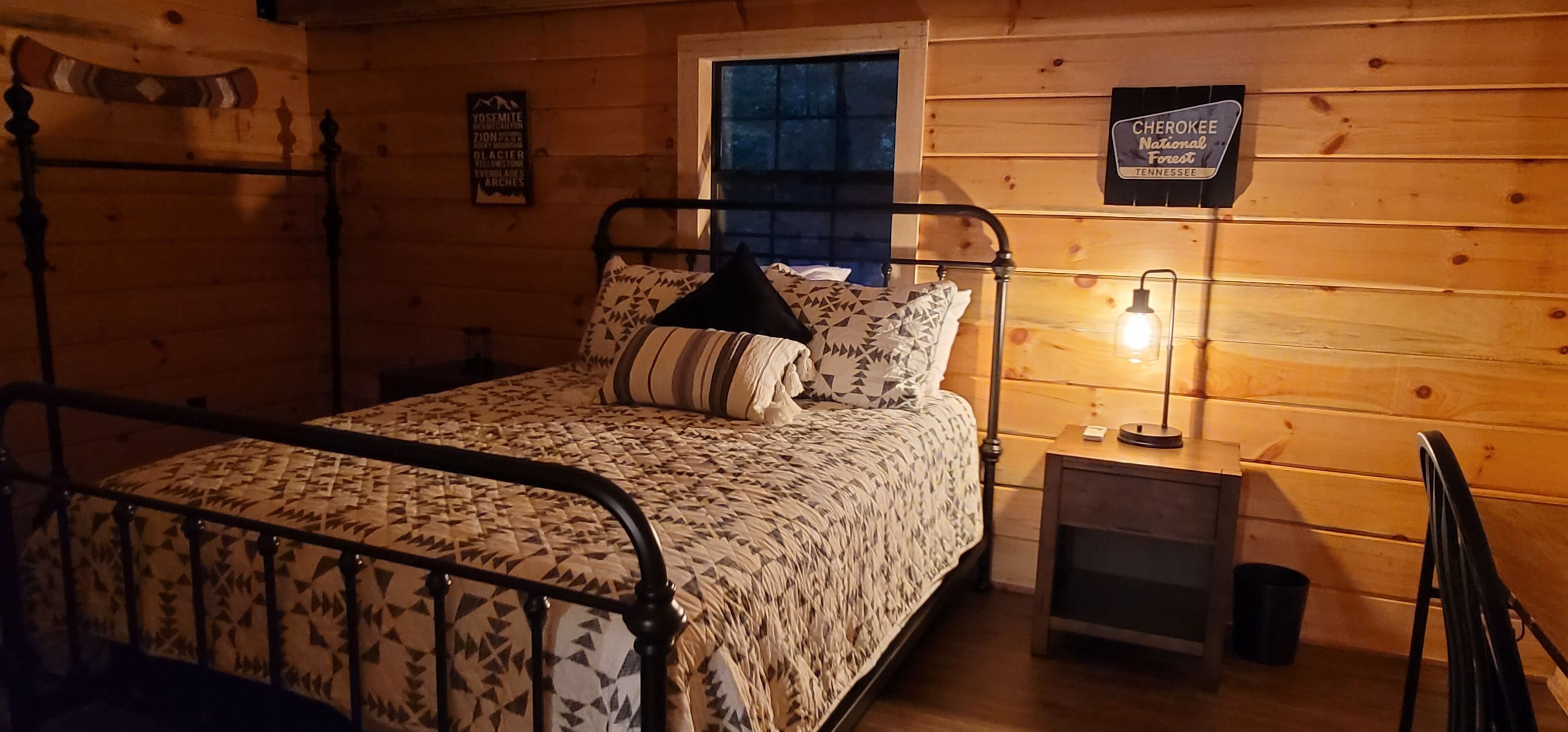 Une pièce de style cabane en bois, avec un lit, une table de chevet, une lampe et un panneau accroché au mur.