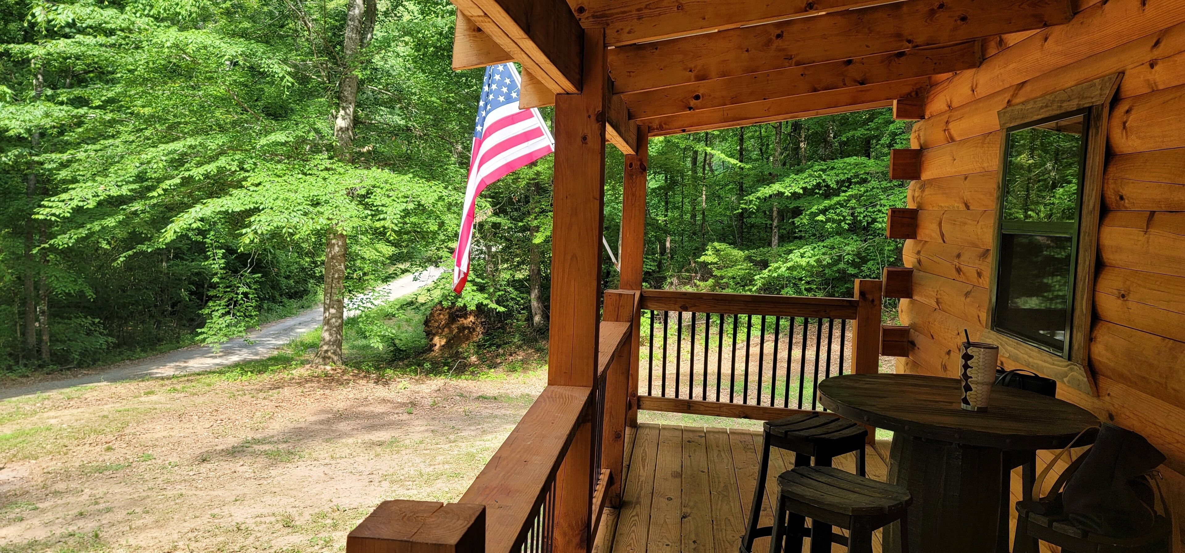 Une cabane en bois avec une véranda, une table et des chaises. On peut voir un drapeau américain.