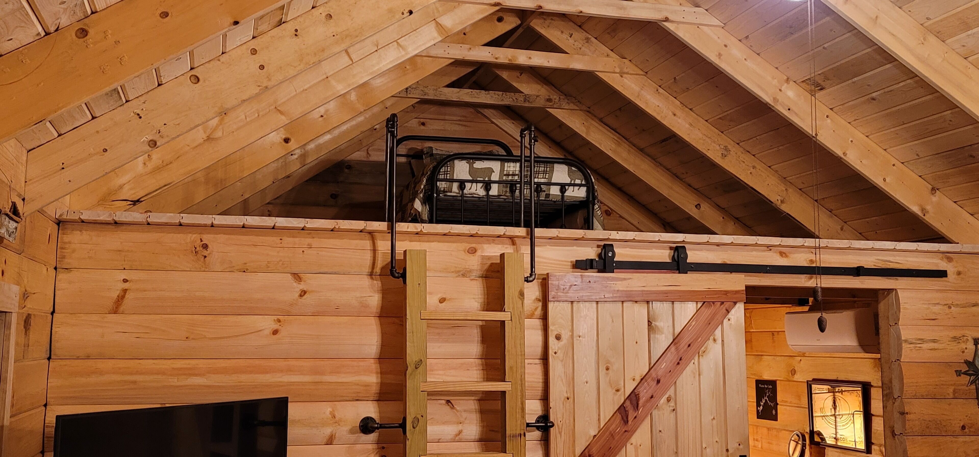 A wooden interior with a lofted sleeping area, a ladder, and a door leading to another room.