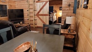 A cozy cabin interior with a fireplace, a television, a dining table, and a bed. - Secluded East TN Log Cabin (Ten Mile)