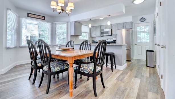 A dining area with a wooden table and chairs, a chandelier, and a kitchen in the background. - ONLY A 7 MINUTE WALK TO THE BEACH! (Bethany Beach)
