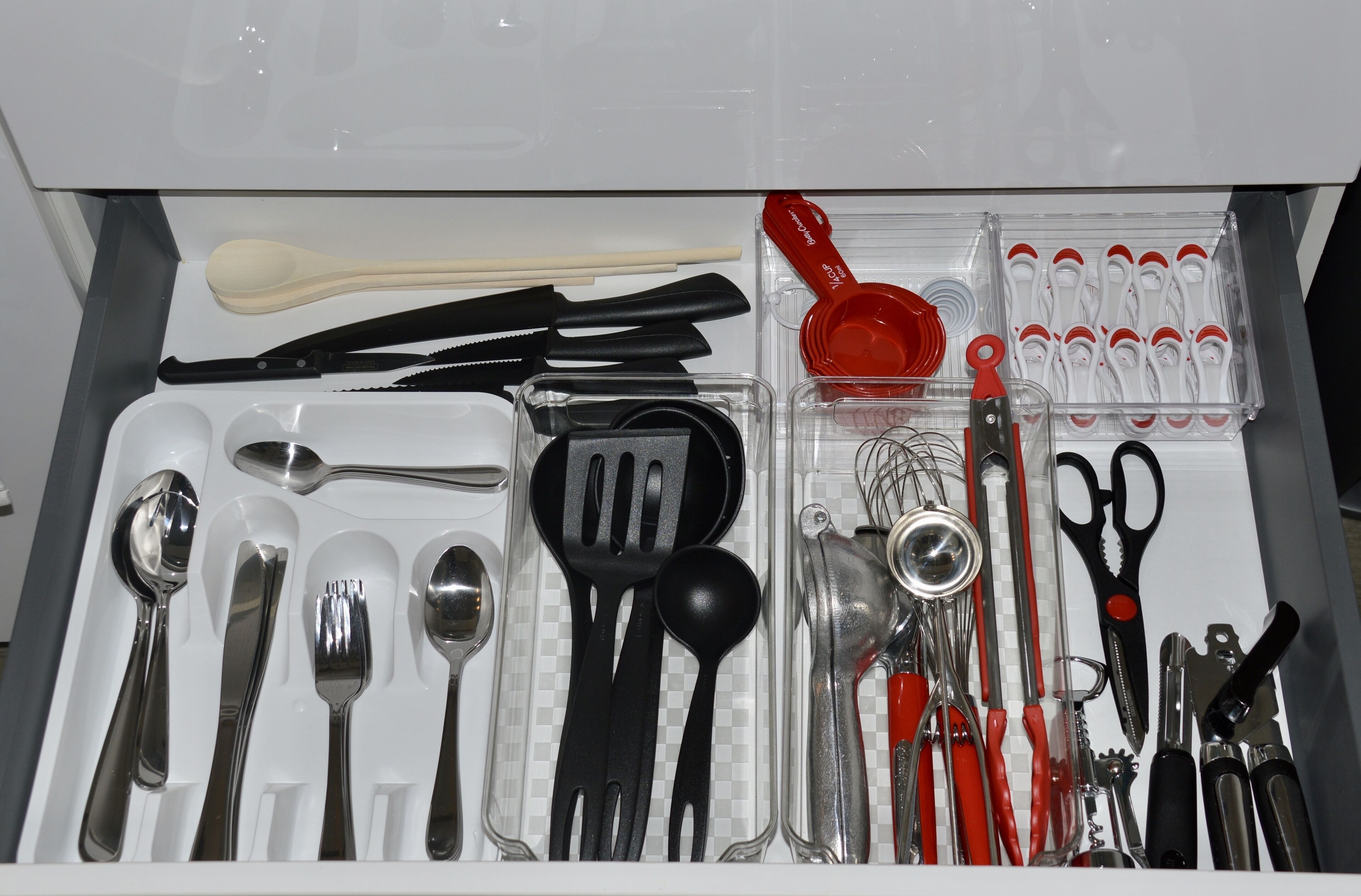 A drawer with various kitchen utensils including spoons, forks, knives, and measuring cups.