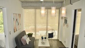 Ein modernes Wohnzimmer mit einem grauen Sofa, einem weißen Couchtisch und einem großen Fenster mit Blick ins Freie.