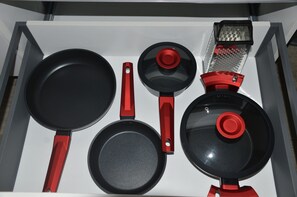 A drawer containing various kitchen utensils including a frying pan, a small pot, and a grater.