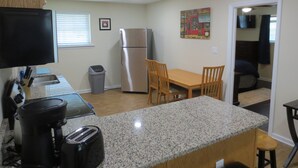 A compact kitchen with a refrigerator, toaster, coffee maker, and a dining area with chairs and a table.