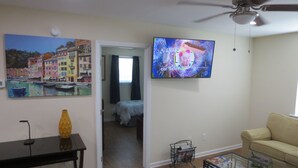 A living room with a sofa, a coffee table, a painting of a harbor, and a television displaying a cartoon.