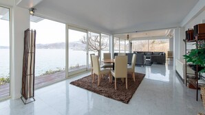 A spacious living area with a large glass door leading to a lake view, a dining area with a table and chairs, and a seating area with a sofa and coffee table.