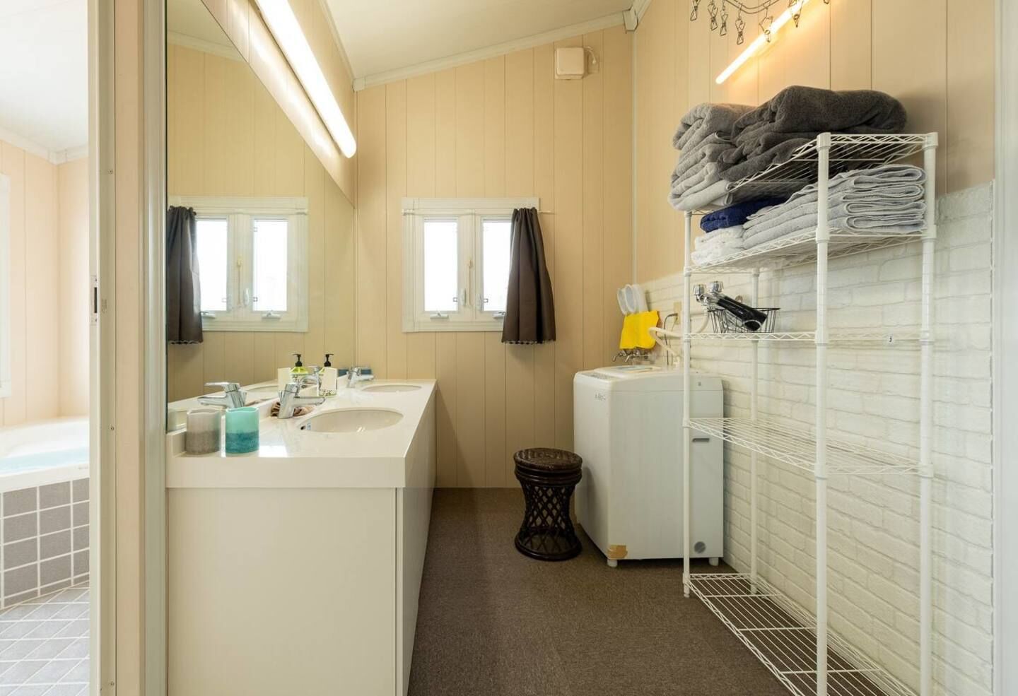 A bathroom with two sinks, a mirror, a towel rack, and a laundry shelf.