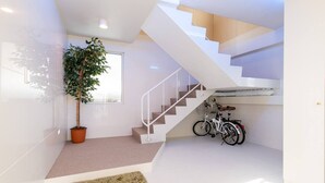 A modern staircase with white railings, a potted plant, and bicycles in a bright, minimally furnished space.