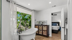 A bathroom with a freestanding bathtub, a cabinet with baskets, and a view of a bedroom with a bed and a nightstand. - Large Home 12 beds Gameroom Heated Salt Pool PPG (Palm Desert)