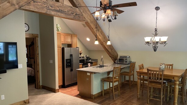 Een moderne keuken met houten balken, een centraal eiland, barstoelen en een eettafel.