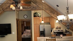 Une cuisine chaleureuse avec des poutres en bois, un coin repas et un salon équipé d’un téléviseur.