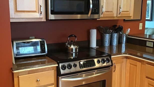 A kitchen with wooden cabinets, a microwave, a toaster, a kettle, and a stove. - Enjoy Northern MN (Cook)