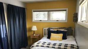 A bedroom with a bed, a nightstand, a lamp, and a window with curtains. - Enjoy Northern MN (Cook)