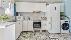 A modern kitchen with white cabinets, a built-in oven, a microwave, and a washing machine. - Kipi Village Zakynthos (Ζάκυνθος)