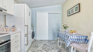 A compact kitchen with a washing machine, a dining table with a checkered tablecloth, and a chair. - Kipi Village Zakynthos (Ζάκυνθος)