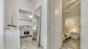 A modern hotel room with a kitchen area, a large mirror, patterned floor tiles, and a bed with a green throw. - Kipi Village Zakynthos (Ζάκυνθο ς)