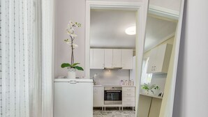 A narrow hallway with patterned floor tiles, a white refrigerator, a potted orchid, and a large mirror on the right. - Kipi Village Zakynthos (Ζάκυνθος)