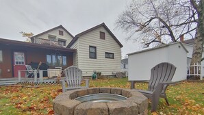 A stone fire pit with two Adirondack chairs, surrounded by fallen leaves. - Huge historic on Lake Michigan w/ large yard, fire pit, BBQ & air conditioning (Manistee)