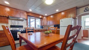 A kitchen with wooden cabinets, a stove, a refrigerator, and a dining table with chairs. - Huge historic on Lake Michigan w/ large yard, fire pit, BBQ & air conditioning (Manistee)