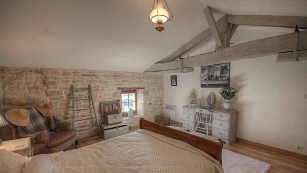 A bedroom with a large bed, a dresser, a chair, and a ladder against a stone wall. - 4Bed3Bath 1736 Farmhouse/Barn Conversion-Hearth (Sainte-Soline)