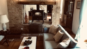 A cozy living room with a stone wall, a fireplace, a sofa, and a coffee table. - 4Bed3Bath 1736 Farmhouse/Barn Conversion-Hearth (Sainte-Soline)