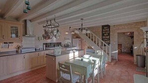 A spacious kitchen with wooden cabinets, a central island, and hanging pots. A staircase leads to a loft area with a stone wall and a sign saying "What I love most about my home is who I made it for." - 4Bed3Bath 1736 Farmhouse/Barn Conversion-Hearth (Sainte-Soline)