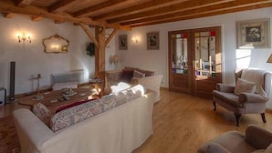 A cozy living room with a wooden ceiling, a sofa, a chair, and a table with decorative items. - 4Bed3Bath 1736 Farmhouse/Barn Conversion-Hearth (Sainte-Soline)