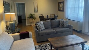 A living room with a gray sofa, a coffee table, a lamp, a dining table with chairs, a potted plant, and a painting on the wall. - Cozy place in heart of Atlanta  (Atlanta)