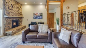 Un salon avec une cheminée en pierre, des canapés en cuir, un tableau et un escalier.