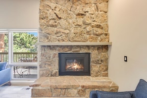 A stone fireplace with a fire, a wooden deck, and a blue sofa. - Deer Mountain Haven! #3560 (Estes Park)