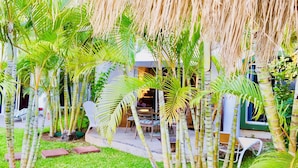 A lush garden with palm trees, a patio area with outdoor furniture, and a building with a green door.
