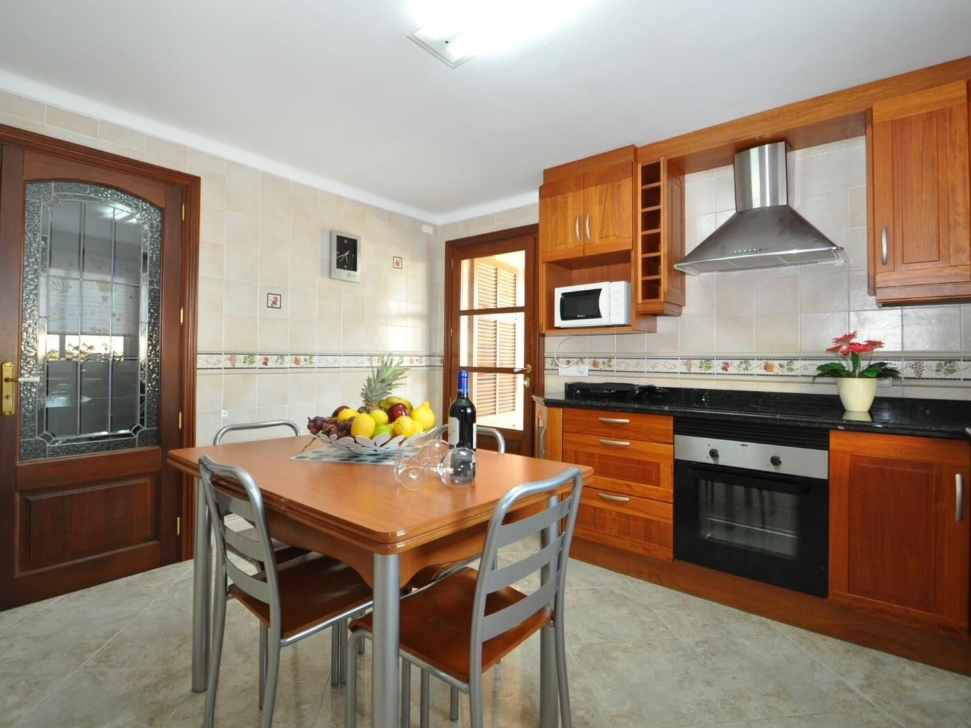 Cocina con armarios de madera, extractor de acero inoxidable, microondas y una mesa de comedor con sillas.