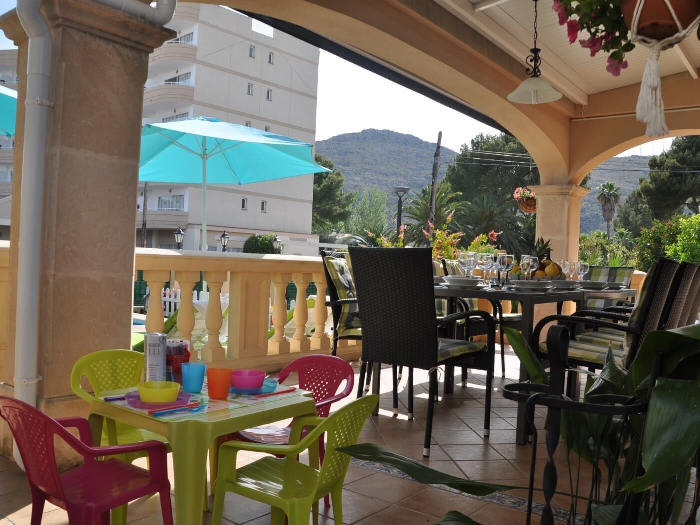 An outdoor dining area with tables and chairs, a blue umbrella, and a view of a mountain.
