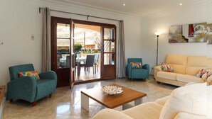 A spacious living room with a large sliding glass door leading to an outdoor area, a wooden coffee table, and two sofas. - Villa Llac Blau – Family, pool & beach Alcudia (Puerto de Alcudia)