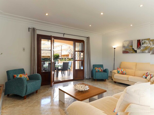 A spacious living room with a large sliding glass door leading to an outdoor area, a wooden coffee table, and two sofas. - Villa Llac Blau – Family, pool & beach Alcudia (Puerto de Alcudia)