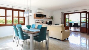 A modern living room with a dining area, a sofa, and a TV. - Villa Llac Blau – Family, pool & beach Alcudia (Puerto de Alcudia)
