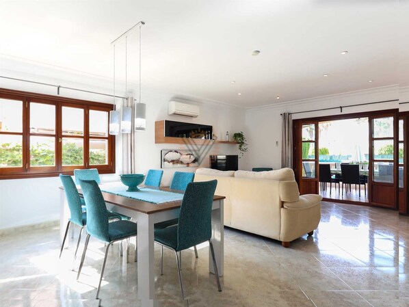 A modern living room with a dining area, a sofa, and a TV. - Villa Llac Blau – Family, pool & beach Alcudia (Puerto de Alcudia)