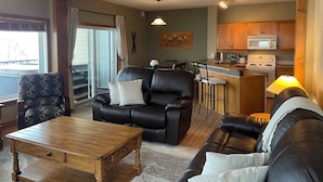 A living room with a leather sofa, a wooden coffee table, and a dining area with a bar. - Kimberley Chalet (Kimberley)