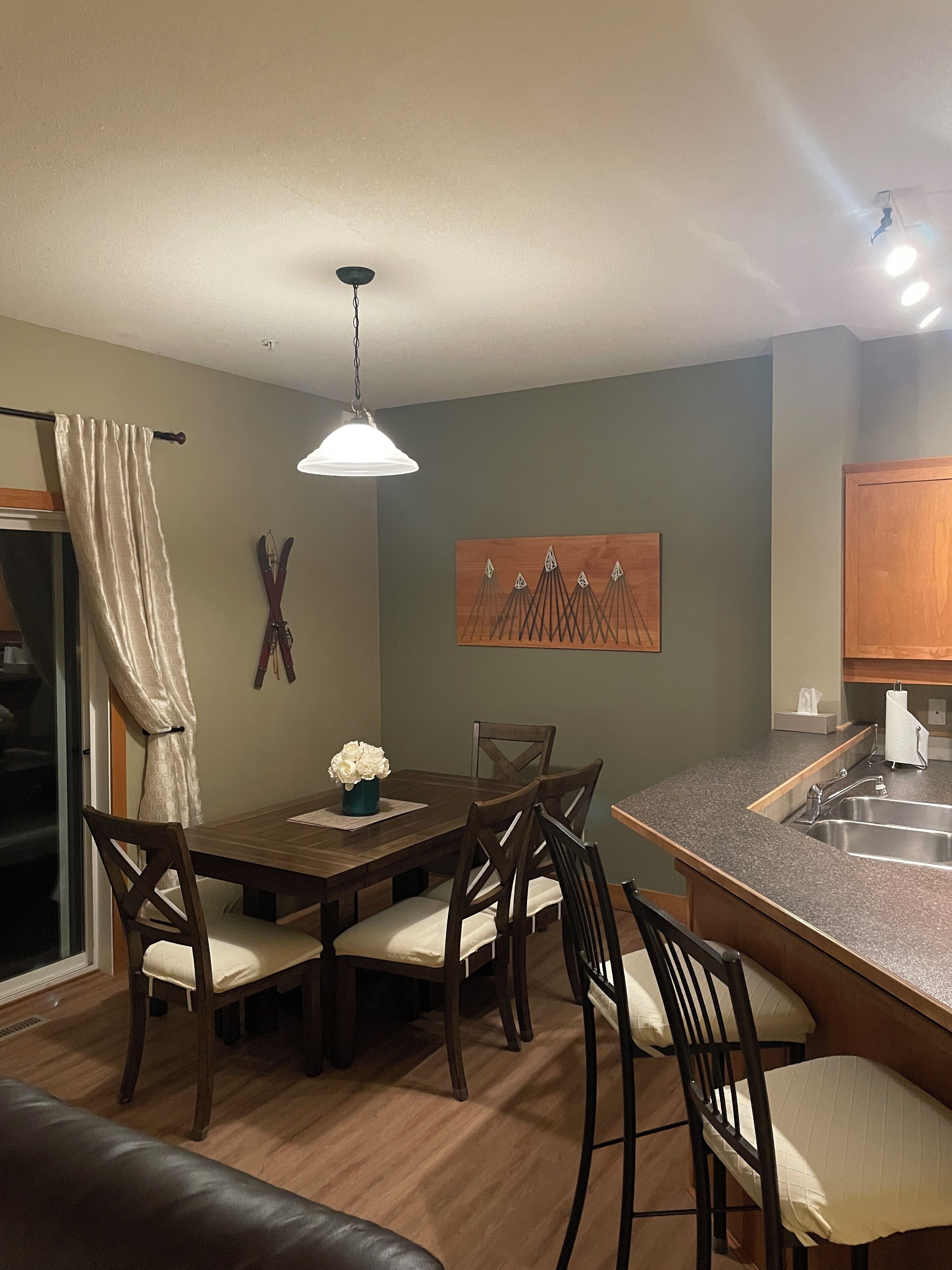 A dining area with a wooden table and chairs, a pendant light, and a kitchen island with a sink.