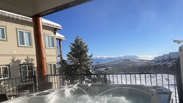 A hot tub with a view of snow-covered mountains and a building with balconies. - Kimberley Chalet (Kimberley)