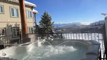 Un bain à remous avec vue sur des montagnes enneigées et un bâtiment doté de balcons.