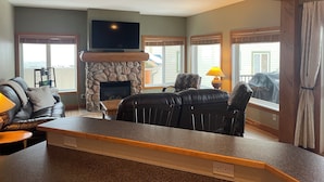 A living room with a stone fireplace, a television mounted above it, and a seating area with a sofa and chairs. - Kimberley Chalet (Kimberley)