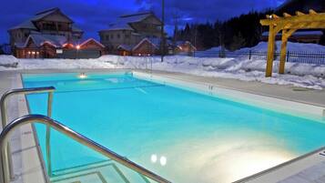 Une piscine à l’eau d’un bleu cristallin, entourée de neige et surmontée d’une pergola en bois.