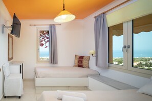 Una camera da letto con due letti, una TV, una finestra con tende e vista mare.